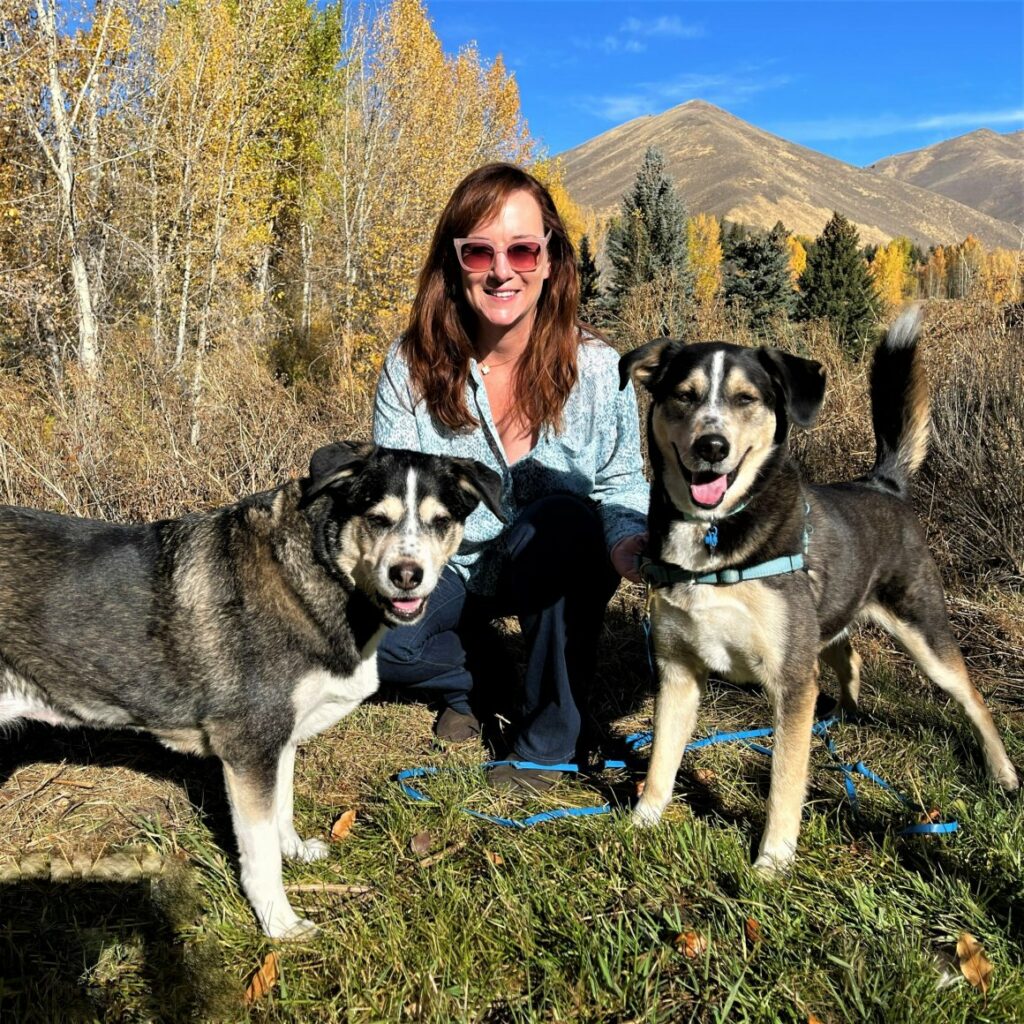 Christine Brumback outdoors posing with her two dogs on either side of her