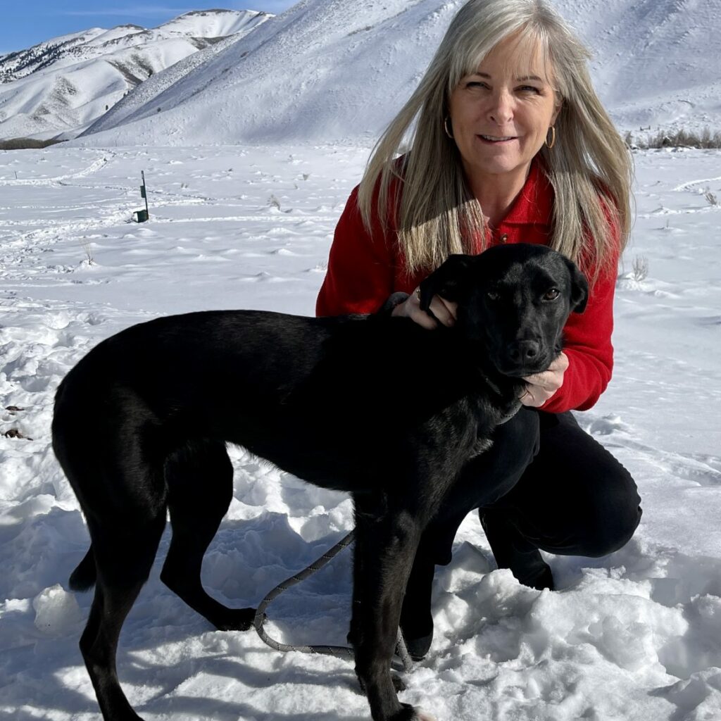 Cheryl Fulton squatting down in the snow while petting her black dog