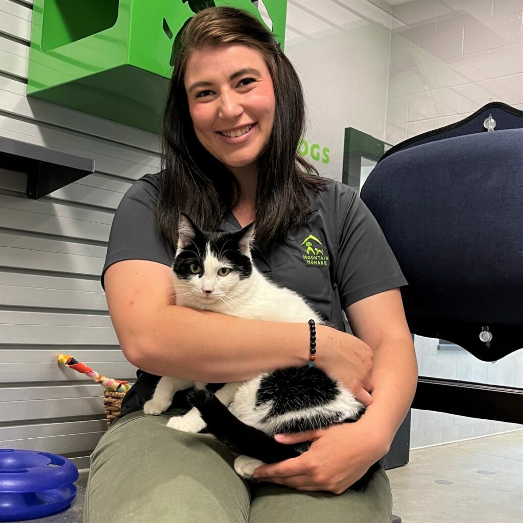 Kadi McGinnis in her Mountain Humane uniform holding black and white cat in her lap